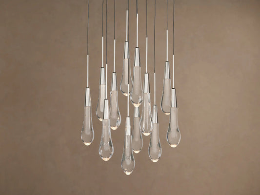 Soltaire Round Chandelier: Clear glass teardrop pendants with metallic caps, glowing, hanging at varied heights on brown background.