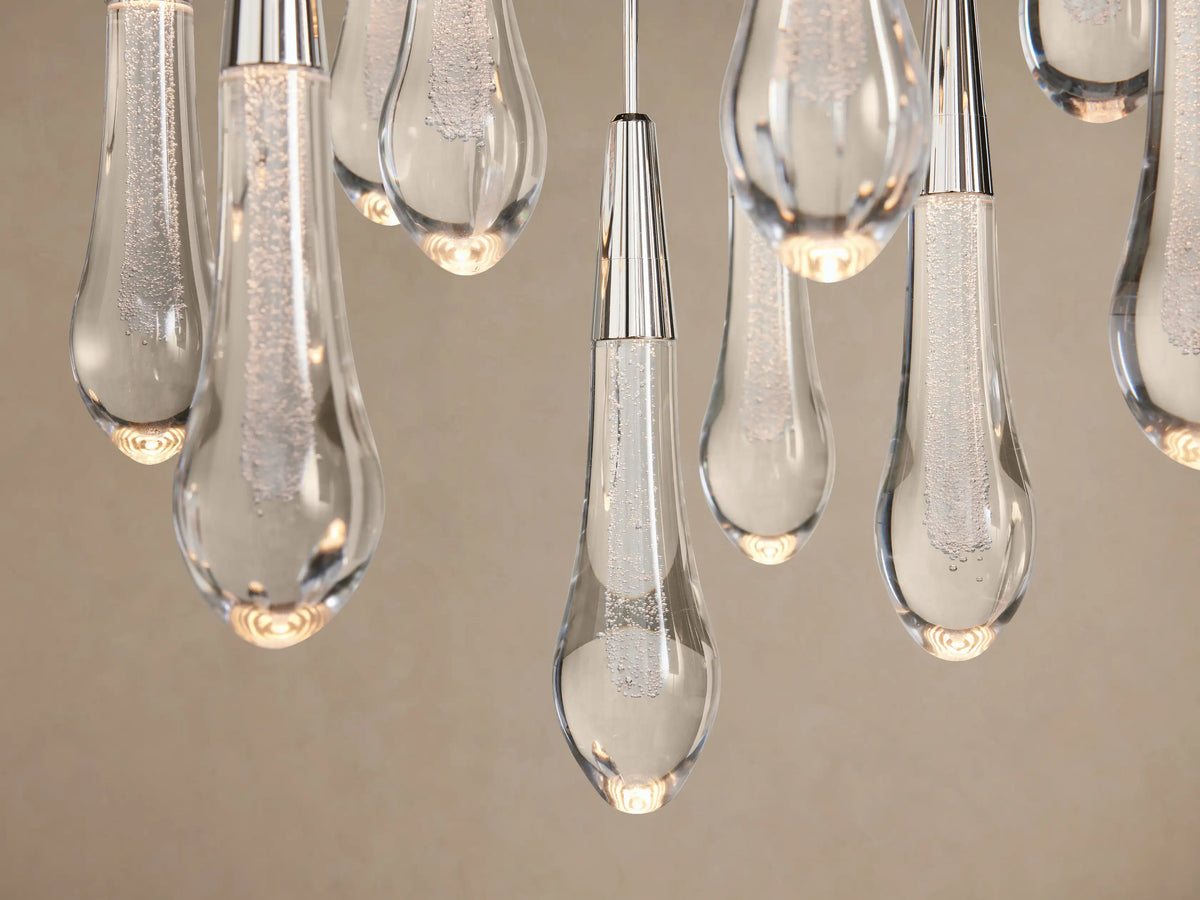 Soltaire Round Chandelier featuring multiple clear glass teardrop pendants with silver caps, hanging against a light brown background.