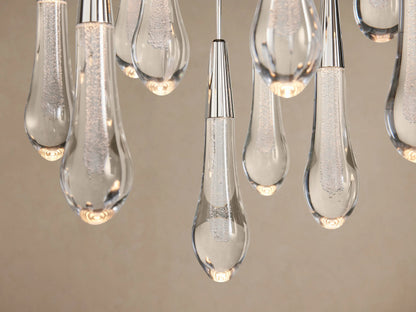Soltaire Round Chandelier featuring multiple clear glass teardrop pendants with silver caps, hanging against a light brown background.