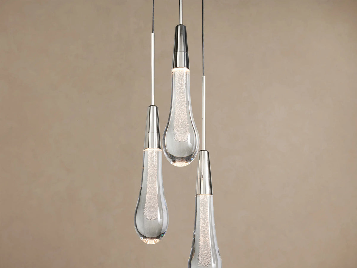 Trio of Soltaire Cluster Pendants with clear, bubbled teardrop glass and silver-toned caps, hanging against a beige wall.