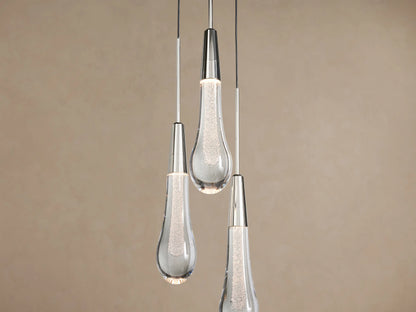 Trio of Soltaire Cluster Pendants with clear, bubbled teardrop glass and silver-toned caps, hanging against a beige wall.