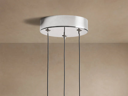 Three illuminated Soltaire Cluster Pendants with clear bubbled glass and polished nickel caps, hanging against a beige wall.
