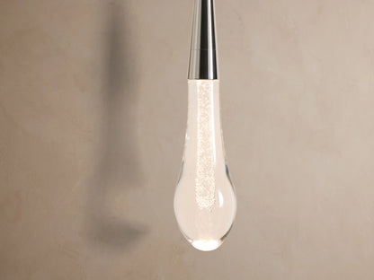 Soltaire Sconce: Round polished nickel backplate with a vertical rod suspending a clear teardrop glass pendant on a light wall.
