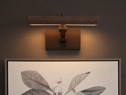 Abel Picture Light Sconce, a dark bronze curved light bar with warm LED light, mounted on a wall above a framed botanical artwork.
