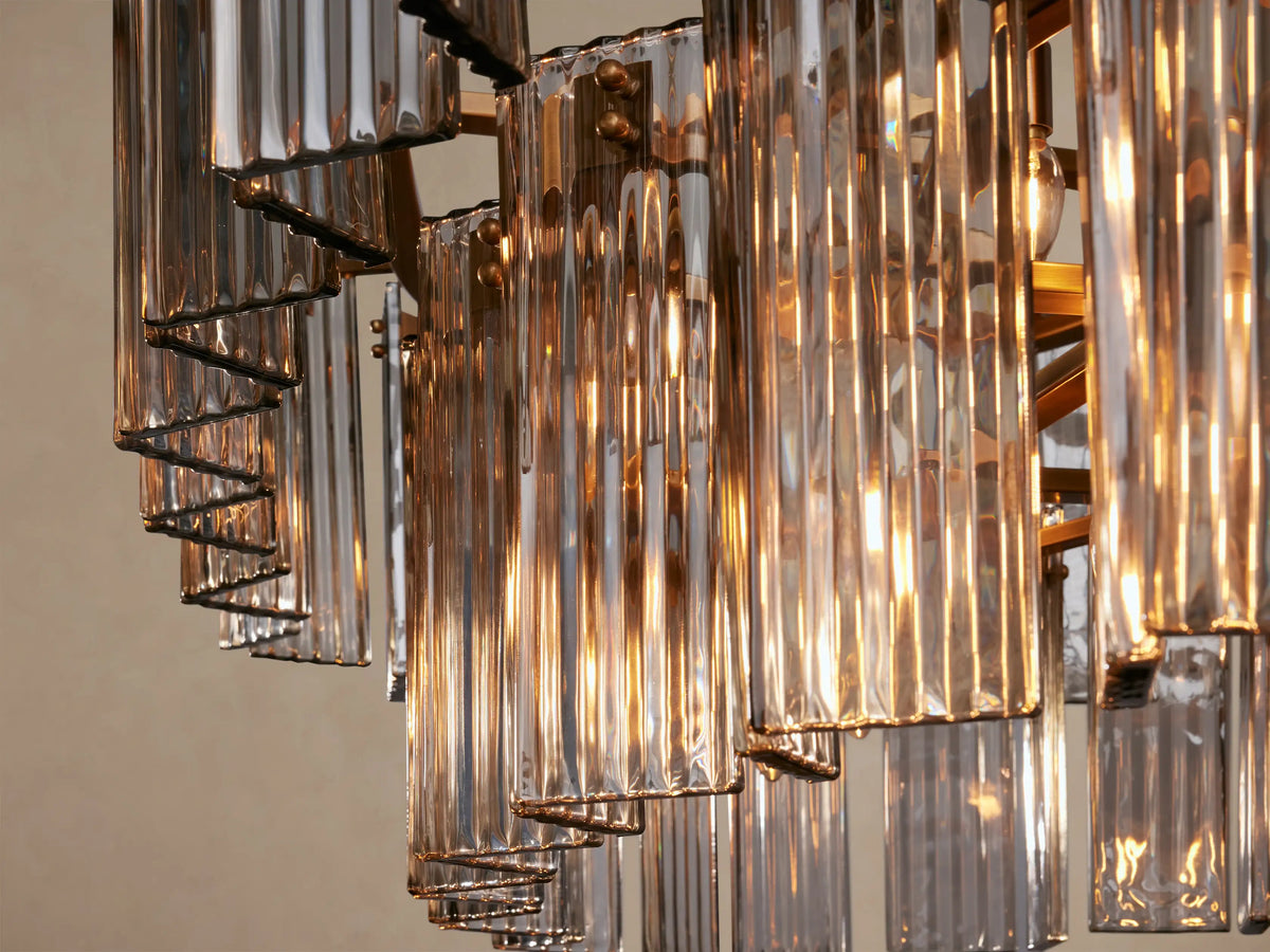 Delsie Oval Tiered Chandelier with two rows of fluted clear glass rods, burnished brass frame, hanging against a beige wall.