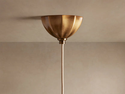 Close-up of Agnes Pendant with antique brass scalloped top, ribbed suspension, and glowing, wavy cream glass shade.