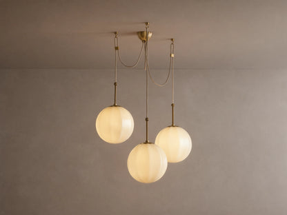 Agnes Chandelier: 3 glowing, paneled cream glass globes suspended from antique brass hardware, draped on a light ceiling.
