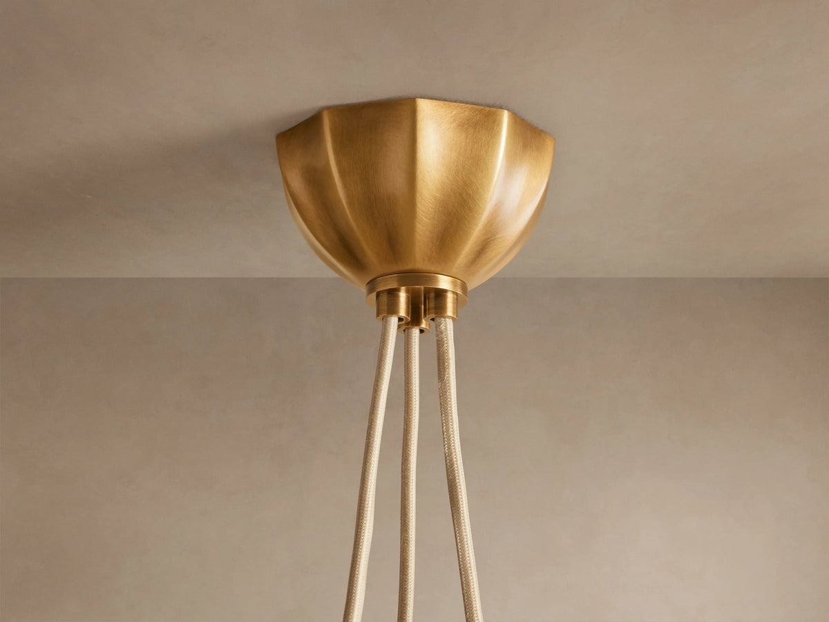 Close-up of Agnes Chandelier. Antique brass hardware with knotted detail and coiled tube above a glowing, cream paneled glass shade.