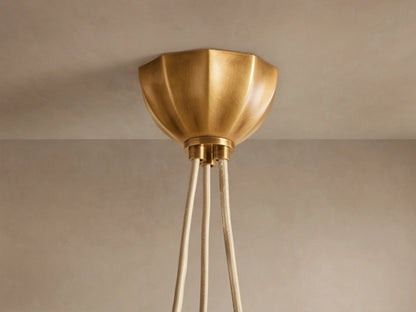 Close-up of Agnes Chandelier. Antique brass hardware with knotted detail and coiled tube above a glowing, cream paneled glass shade.