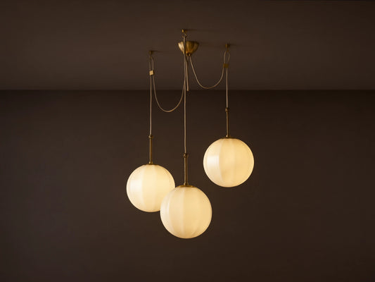 Agnes Chandelier: 3 glowing, paneled cream glass globes suspended from antique brass hardware, draped on a light ceiling.