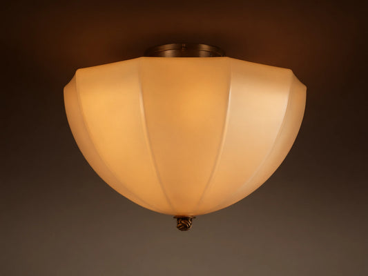 Agnes Flush Mount with paneled cream glass shade & antique brass details, emitting a warm glow from a ceiling mount.