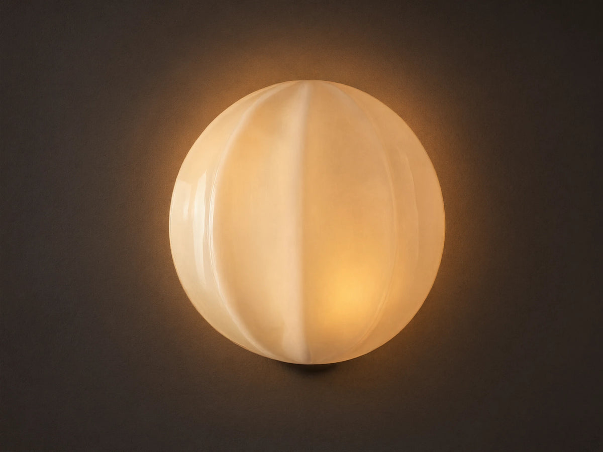 Agnes Clamshell Sconce: Spherical cream paneled glass sconce, glowing warmly, mounted on a light wall next to a dark mirror.