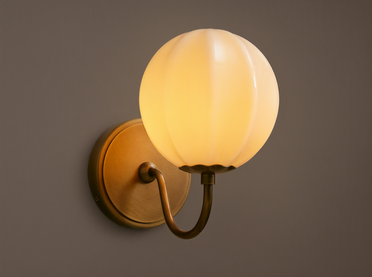 Agnes Gooseneck Sconce with antique brass base, curved arm, and glowing paneled cream glass globe shade mounted on a wall.