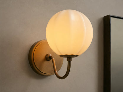 Agnes Gooseneck Sconce with antique brass base, curved arm, and glowing paneled cream glass globe shade mounted on a wall.