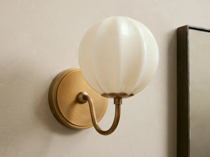 Agnes Gooseneck Sconce with antique brass base, curved arm, and glowing paneled cream glass globe shade mounted on a wall.
