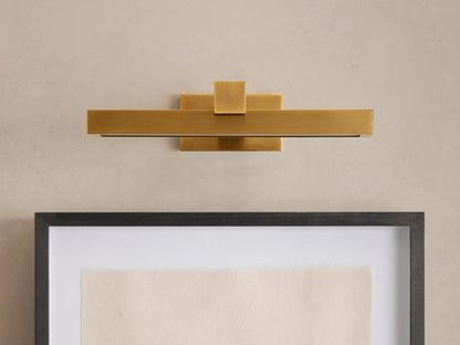 Corinth Picture Light Sconce, brass rectangular bar with LED light, mounted on wall above framed art.