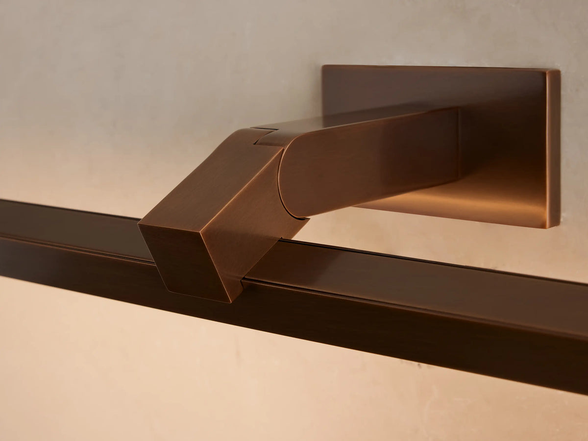 Corinth Picture Light Sconce: a bronze rectangular bar light mounted on a beige wall, positioned above a framed abstract artwork.