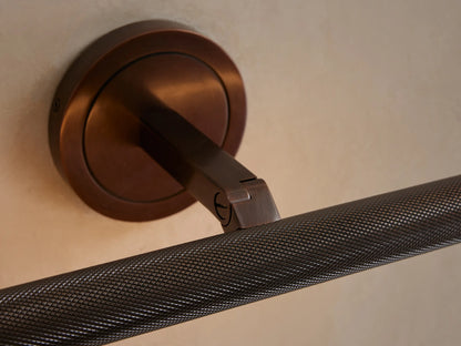 Close-up of a Monroe Picture Light Sconce in antique brass with knurled detailing, mounted on a light wall, light glowing below.