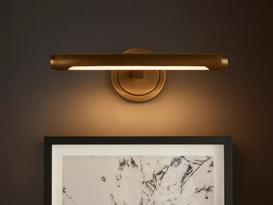Monroe Picture Light Sconce in antique brass, emitting warm LED light over a framed abstract artwork on a light-colored wall.