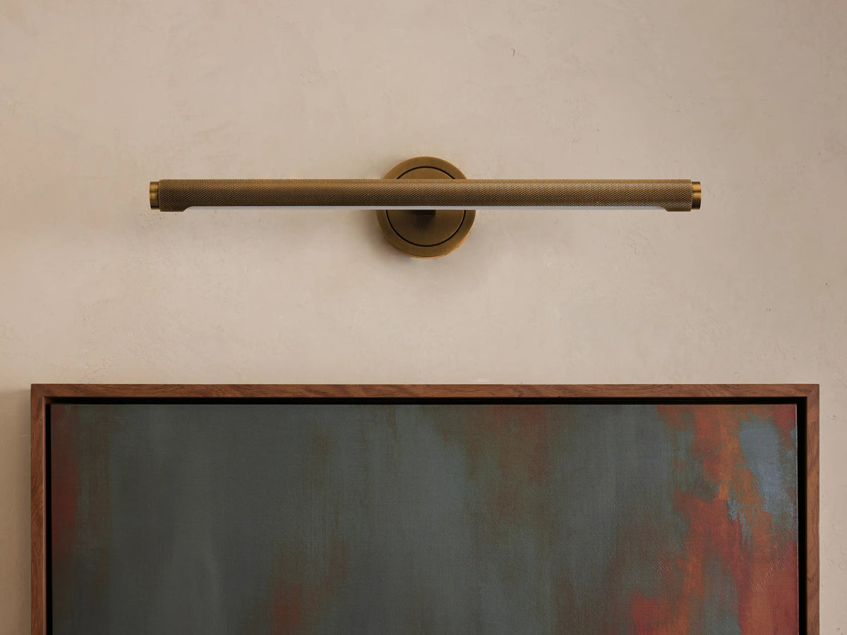 Antique brass knurled Monroe Picture Light Sconce mounted horizontally above a framed abstract painting on a light wall.