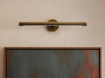 Antique brass knurled Monroe Picture Light Sconce mounted horizontally above a framed abstract painting on a light wall.