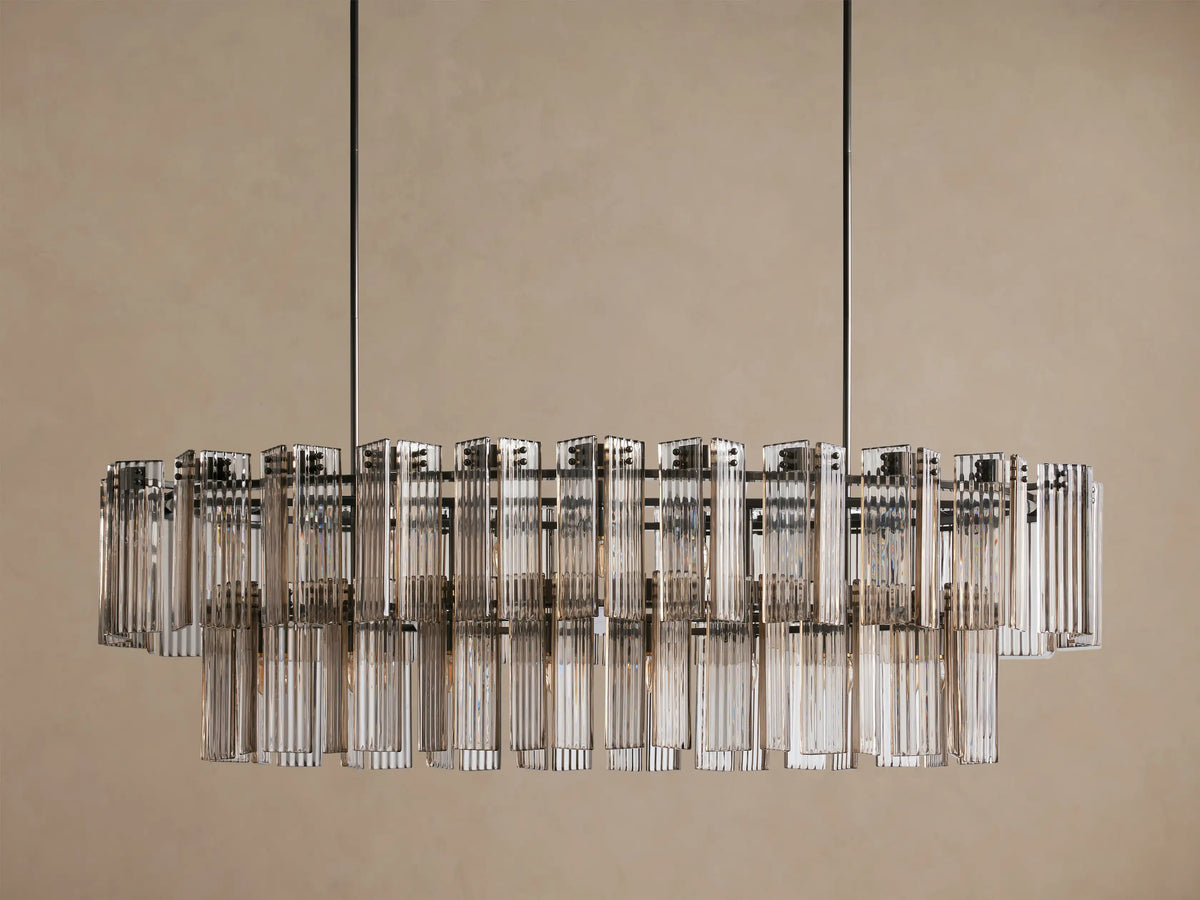 Oval Delsie Chandelier: Dark burnished frame, two tiers of illuminated fluted glass rods suspended against a warm beige wall.