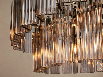 Delsie Oval Tiered Chandelier featuring two rows of smoky rectangular glass rods and a dark metal frame on a plain background.