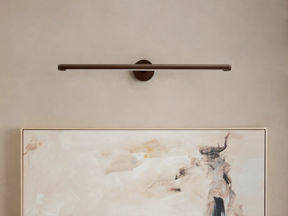 Monroe Picture Light Sconce in antique brass, linear design mounted above a light-colored abstract painting on a beige wall.