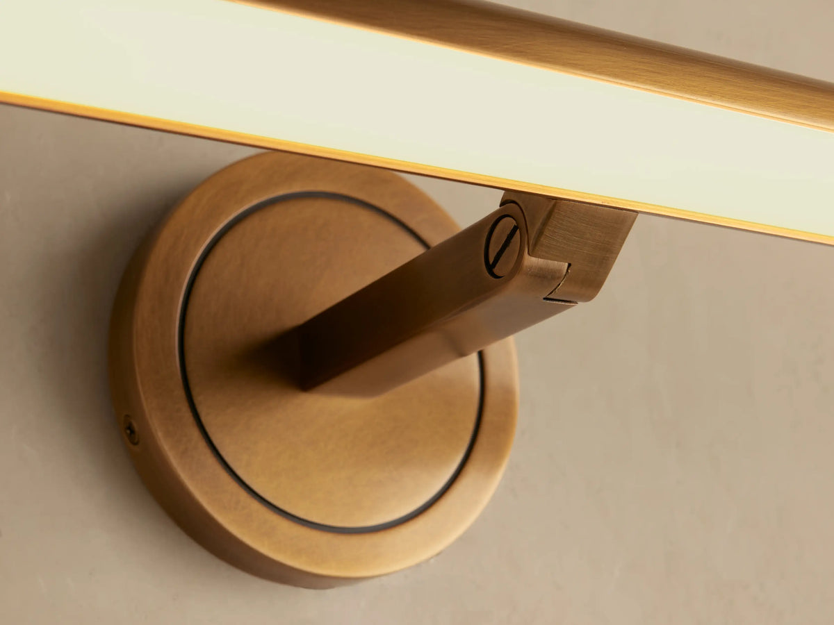 Close-up of Monroe Picture Light Sconce in antique brass, mounted on a wall, with illuminated warm LED light strip.