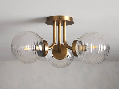 The Sayre Flush Mount features three ribbed glass globes on a burnished brass fixture, mounted flush to a ceiling.