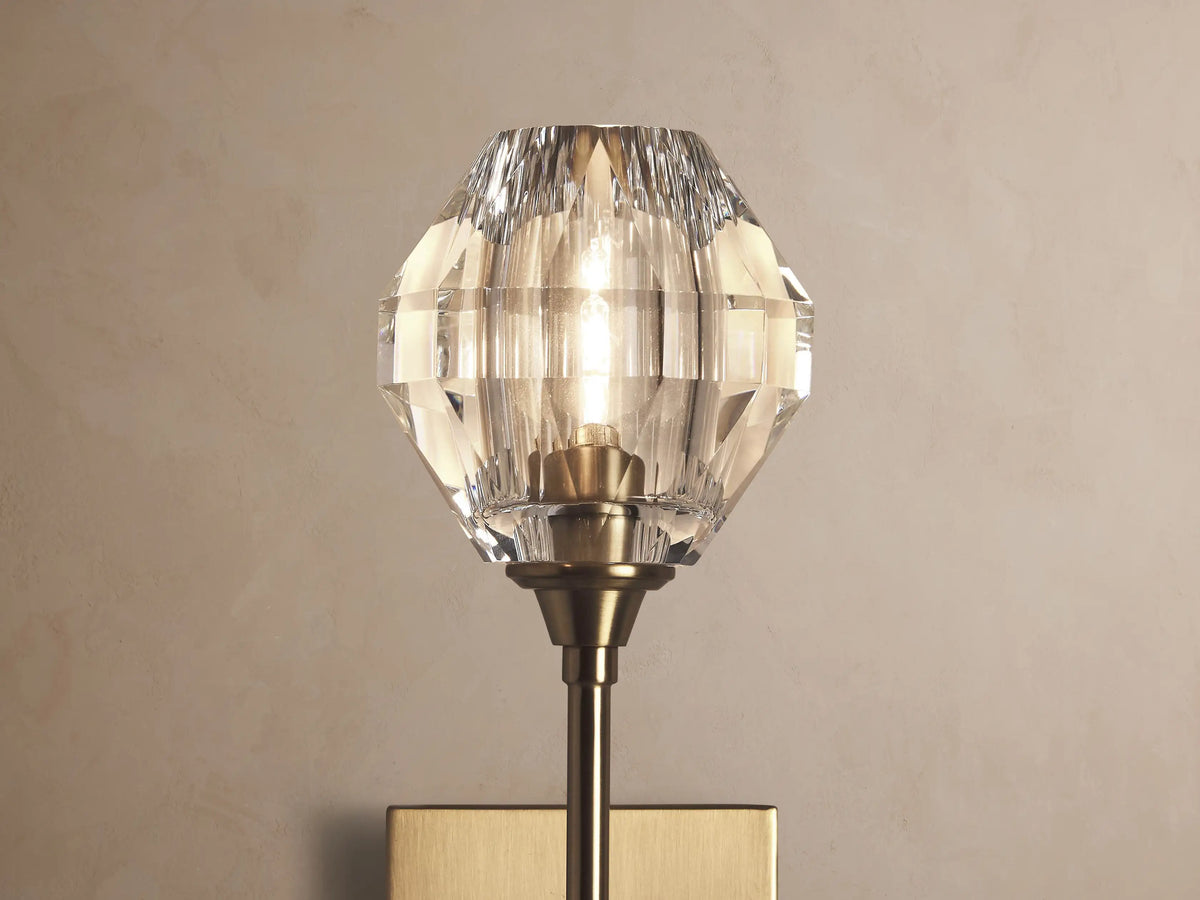 Amoroso Sconce: brass-plated wall-mounted fixture with a long arm, topped by a faceted clear crystal element.