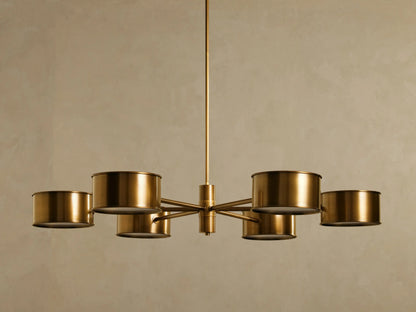 Daphne Metal Round Chandelier with 6 antique brass cylindrical metal shades radiating from a central rod, glowing softly.