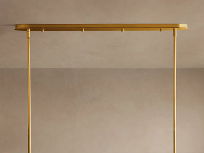 Close-up of Daphne Metal Linear Chandelier. Multiple antique brass drum shades glow warmly, some illuminated.