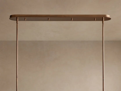 Close-up of a Daphne Metal Linear Chandelier. Several warm bronze metal shades emit bright light, one tilted to show its interior.