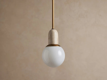 Christie Pendant light hanging. Features a brass rod, natural gray stone cap, and a glowing spherical milk glass shade.