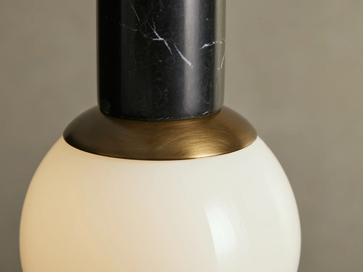 Christie Pendant: Hanging light with a brass rod, black marbled stone top, and spherical white milk glass shade.