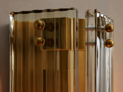 Delsie Sconce, a vertical fluted glass and burnished brass wall light, mounted on a grey wall next to a dark-framed mirror.