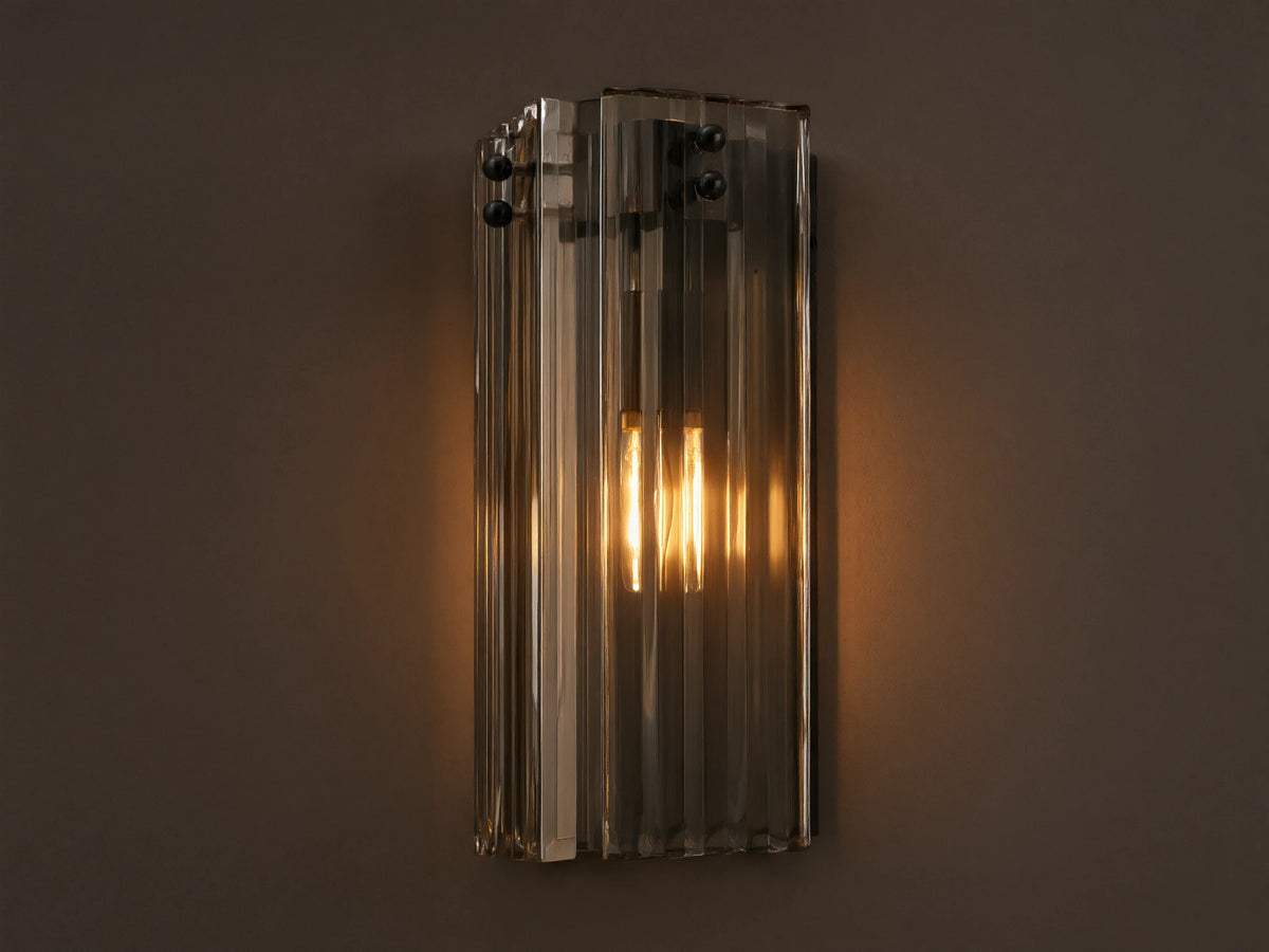 Delsie Sconce: Vertical light with ribbed smoky glass, dark metal frame, and two glowing bulbs, on a light wall beside a mirror.