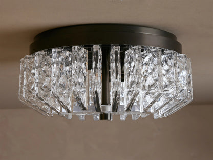 Liliana Flush Mount with a dark metal base and textured clear glass panels glowing with warm light, mounted on a ceiling.
