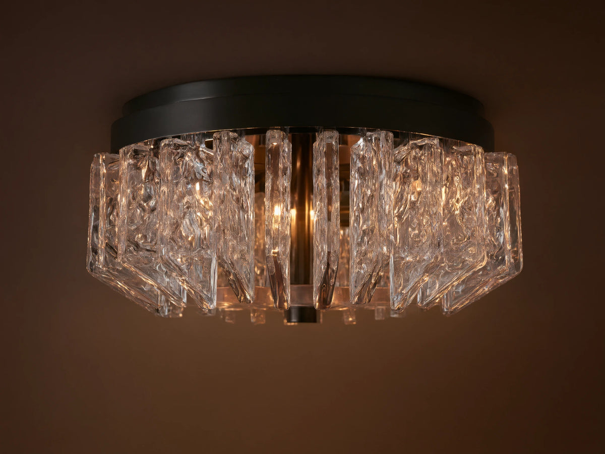 Liliana Flush Mount with a dark metal base and textured clear glass panels glowing with warm light, mounted on a ceiling.