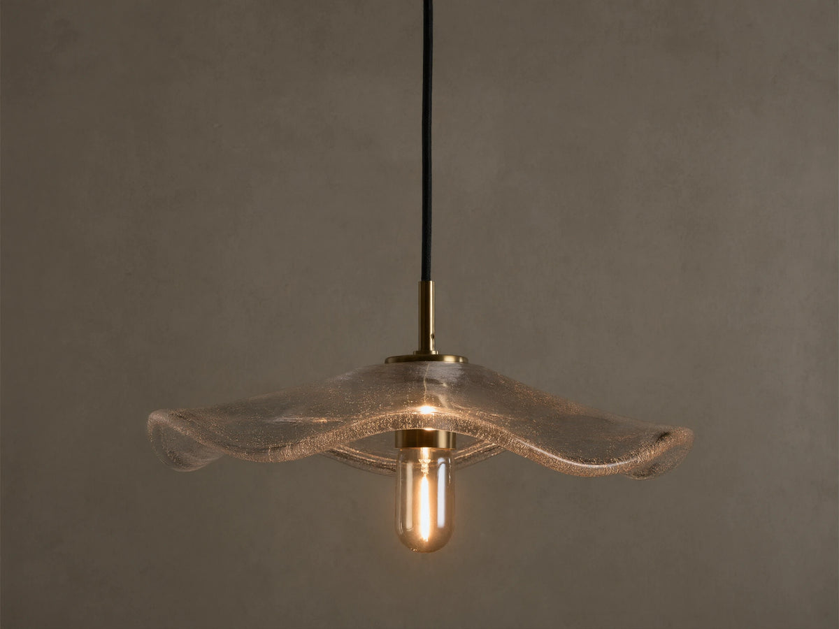 Front view of a clear wavy glass pendant light with a brass fixture and an exposed filament bulb, hanging from a black cord.