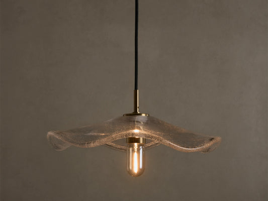 Front view of a clear wavy glass pendant light with a brass fixture and an exposed filament bulb, hanging from a black cord.