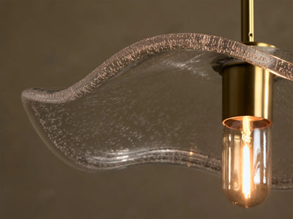 Front view of the clear ripple-effect glass pendant light, with a brass fitting, black fabric cord, and exposed filament bulb.