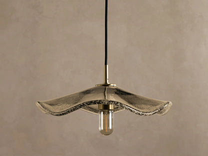 Close-up of a pendant light with a textured, iridescent antique glass shade, brass stem, and a warm-glowing filament bulb.