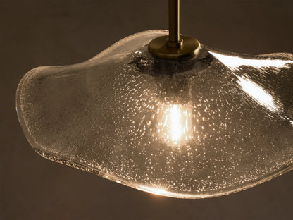 Front view of a wavy, textured smoky glass pendant light with brass hardware, an exposed filament bulb, and black cord.
