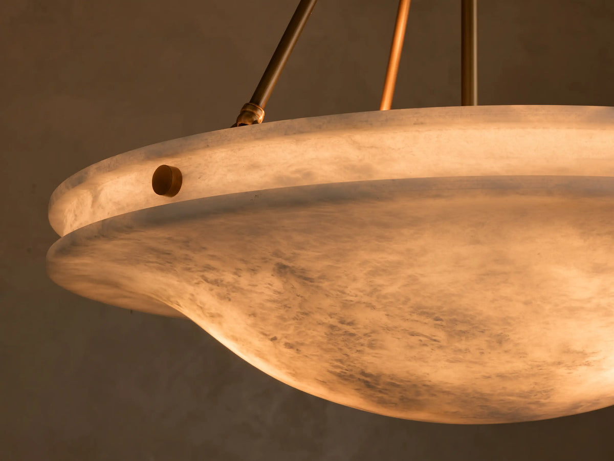 Front view of the Edith Pendant with an illuminated wavy alabaster stone shade and brass-finished suspension rods.
