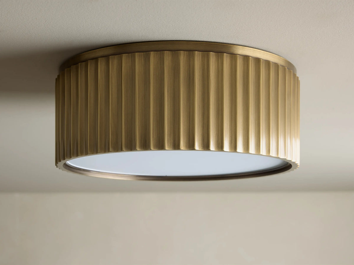 Upward view of a glowing brass ribbed flush mount ceiling light fixture against a white ceiling.