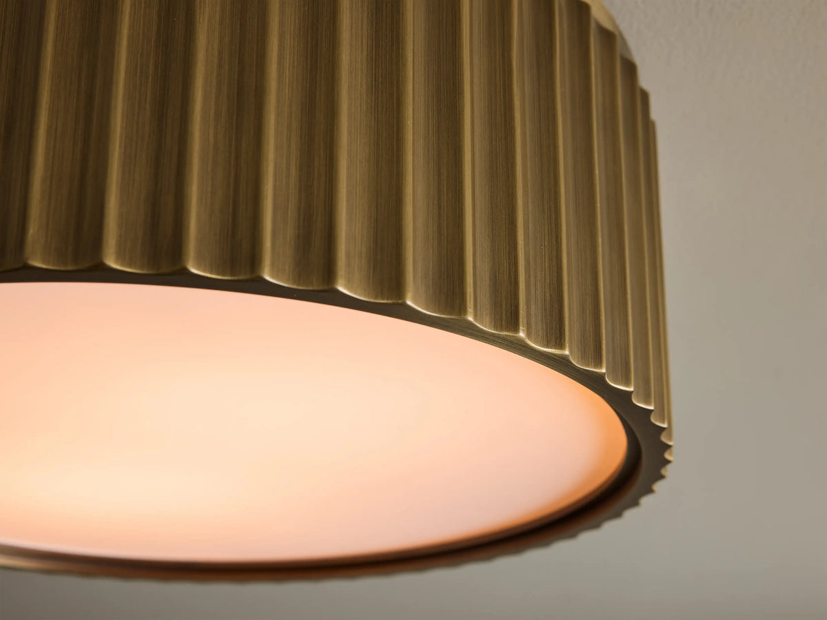 Front view of a brass cylindrical flush mount ceiling light with vertical fluted details and a white diffuser.