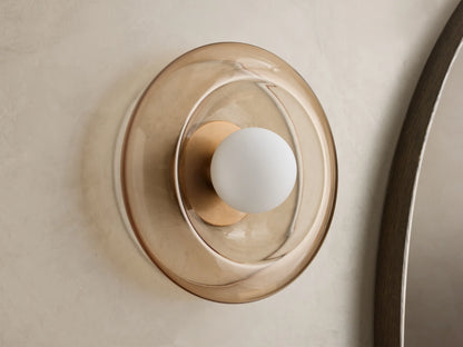 Front view of a wall sconce with a sculpted round amber glass shade, a brass-toned base, and a white globe bulb.
