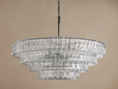 Ghiaccio Round Chandelier, multi-tiered with clear, textured curved glass pieces, hanging from a dark chain against a beige wall.